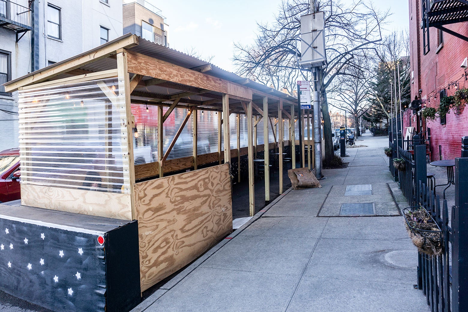 An outdoor dining shed made of unfinished plywood butts up against a sidewalk in New York.